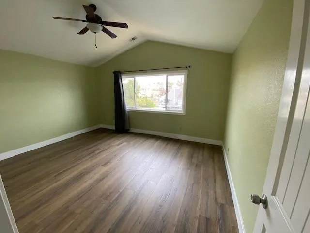 an empty room with wooden floor fan and windows