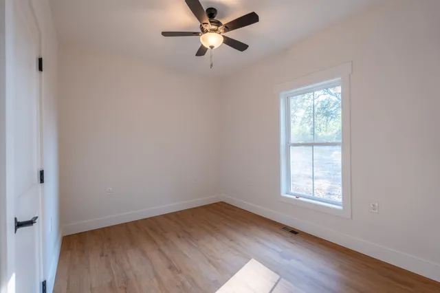 an empty room with wooden floor ceiling fan and windows