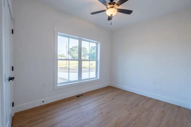 an empty room with wooden floor fan and windows