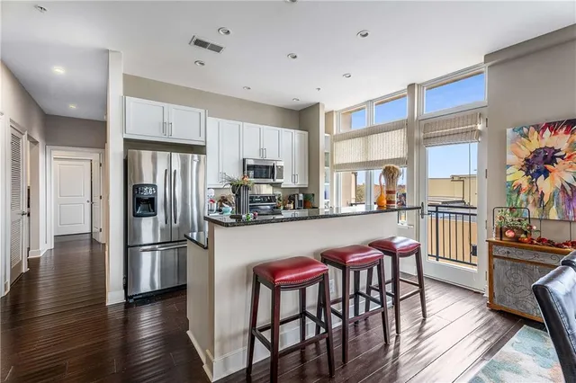 a kitchen with stainless steel appliances granite countertop a refrigerator a stove a sink a dining table and chairs with wooden floor