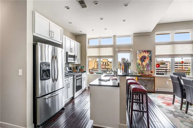a kitchen with stainless steel appliances granite countertop a refrigerator a stove top oven a sink dishwasher and white cabinets with wooden floor