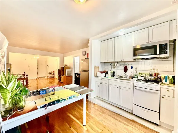 a kitchen with stainless steel appliances kitchen island granite countertop a sink dishwasher stove and white cabinets with wooden floor