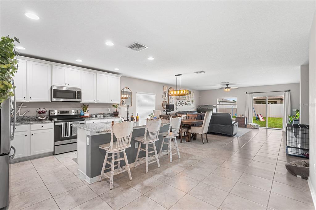 12960 Conquistador Loop Spring Hill, FL 34610 - Photo 5 of 26 a kitchen with stainless steel appliances kitchen island granite countertop a table chairs microwave and sink