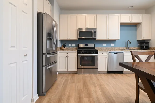 a kitchen with stainless steel appliances a stove a sink a refrigerator with white cabinets and wooden floor