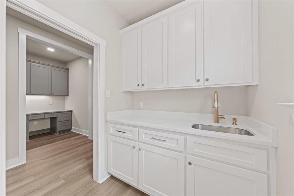 9824 Durango Trail Waco, TX 76712 - Photo 12 of 30 Bar with built in desk, light stone counters, light wood-style floors, and dual tone cabinets