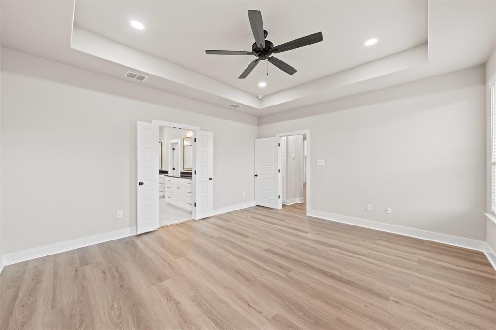 9824 Durango Trail Waco, TX 76712 - Photo 23 of 30 Unfurnished bedroom with a ceiling fan, light wood-style flooring, recessed lighting, ensuite bath, and a tray ceiling