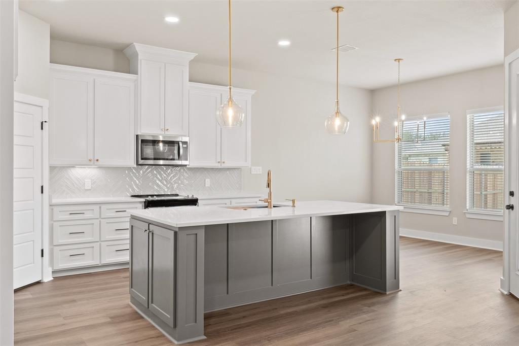 9824 Durango Trail Waco, TX 76712 - Photo 7 of 30 Kitchen with backsplash, light wood-style flooring, two tone cabinetry, a kitchen island with sink, and stainless steel microwave