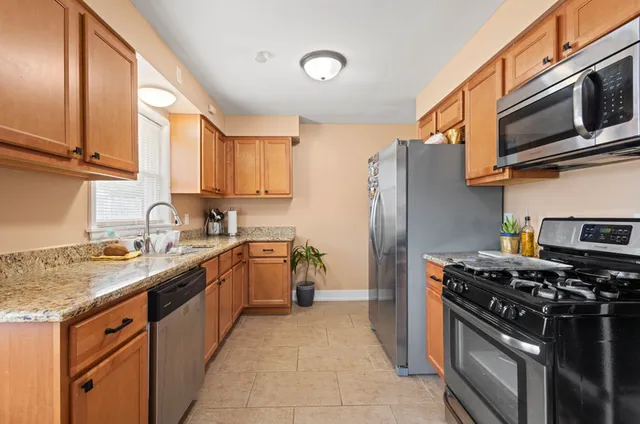 a kitchen with stainless steel appliances granite countertop a stove top oven a sink dishwasher and a refrigerator with wooden cabinets