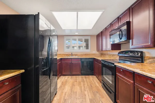 a kitchen with stainless steel appliances granite countertop a refrigerator a sink dishwasher a stove and white countertops with wooden floor