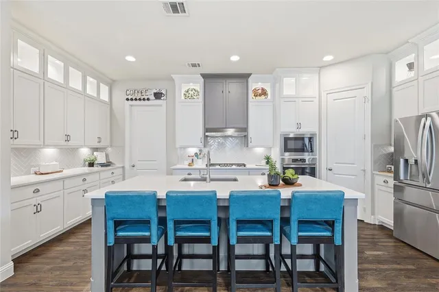 a kitchen with stainless steel appliances kitchen island granite countertop a dining table chairs and a refrigerator