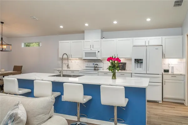 a kitchen with stainless steel appliances kitchen island granite countertop a dining table chairs refrigerator and microwave