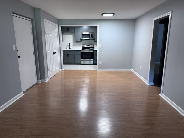 an empty room with wooden floor and a kitchen