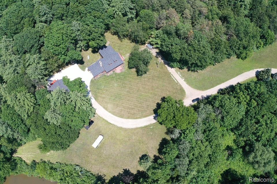 3656 Stanley Road Columbiaville, MI 48421 - Photo 54 of 65 Wooded setting featuring a single-story residence with dark shingle roofing, gravel driveway, and surrounding green space