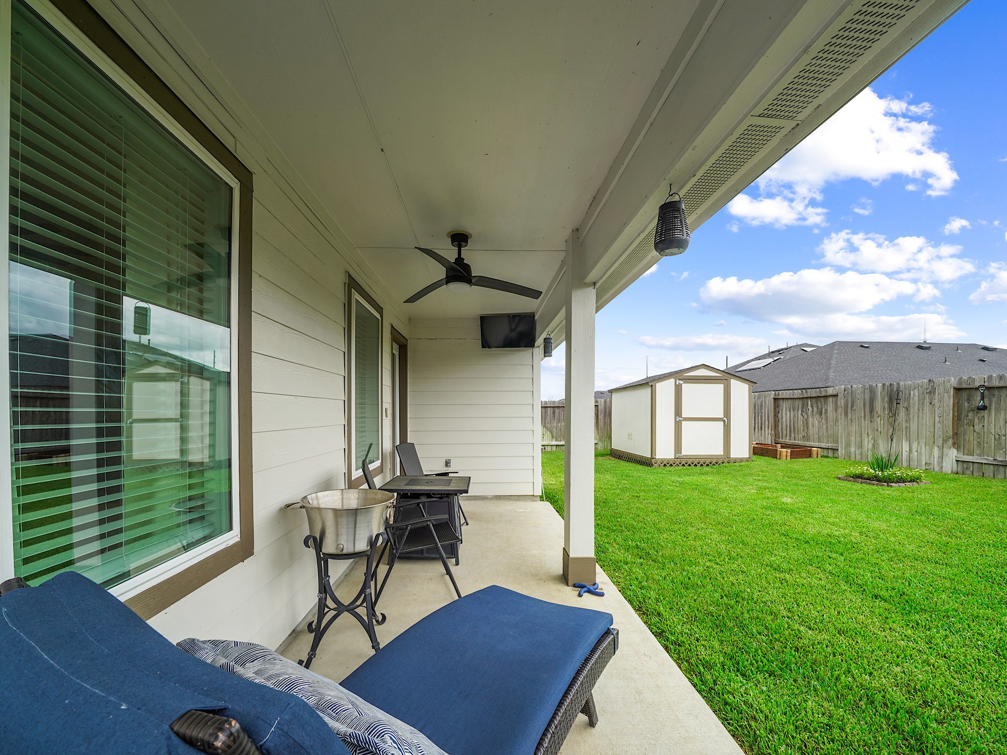 7823 Cattlewood Pass Rosharon, TX 77583 - Photo 16 of 17 Covered patio with a ceiling fan, and a TV, overlooking the backyard with a storage shed, perfect for outdoor relaxation and entertaining.