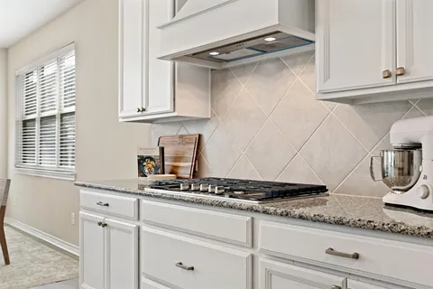 a kitchen with granite countertop stainless steel appliances white cabinets and a window