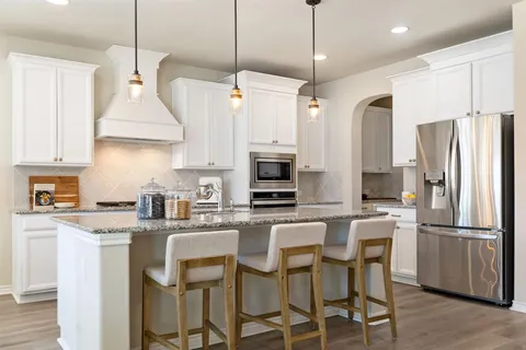 a kitchen with stainless steel appliances a dining table chairs refrigerator and microwave