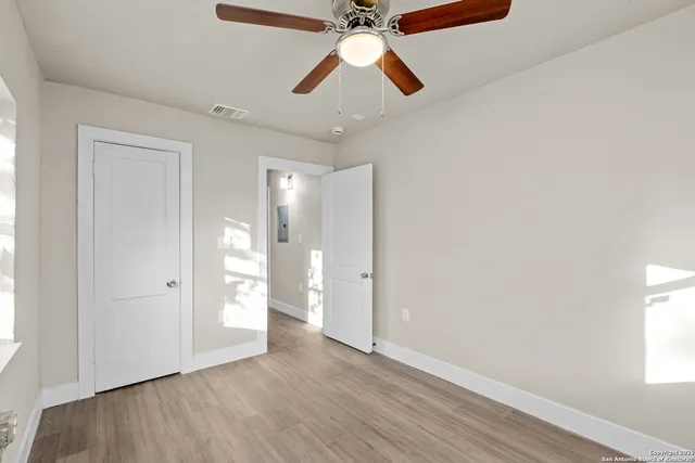 an empty room with wooden floor ceiling fan and windows