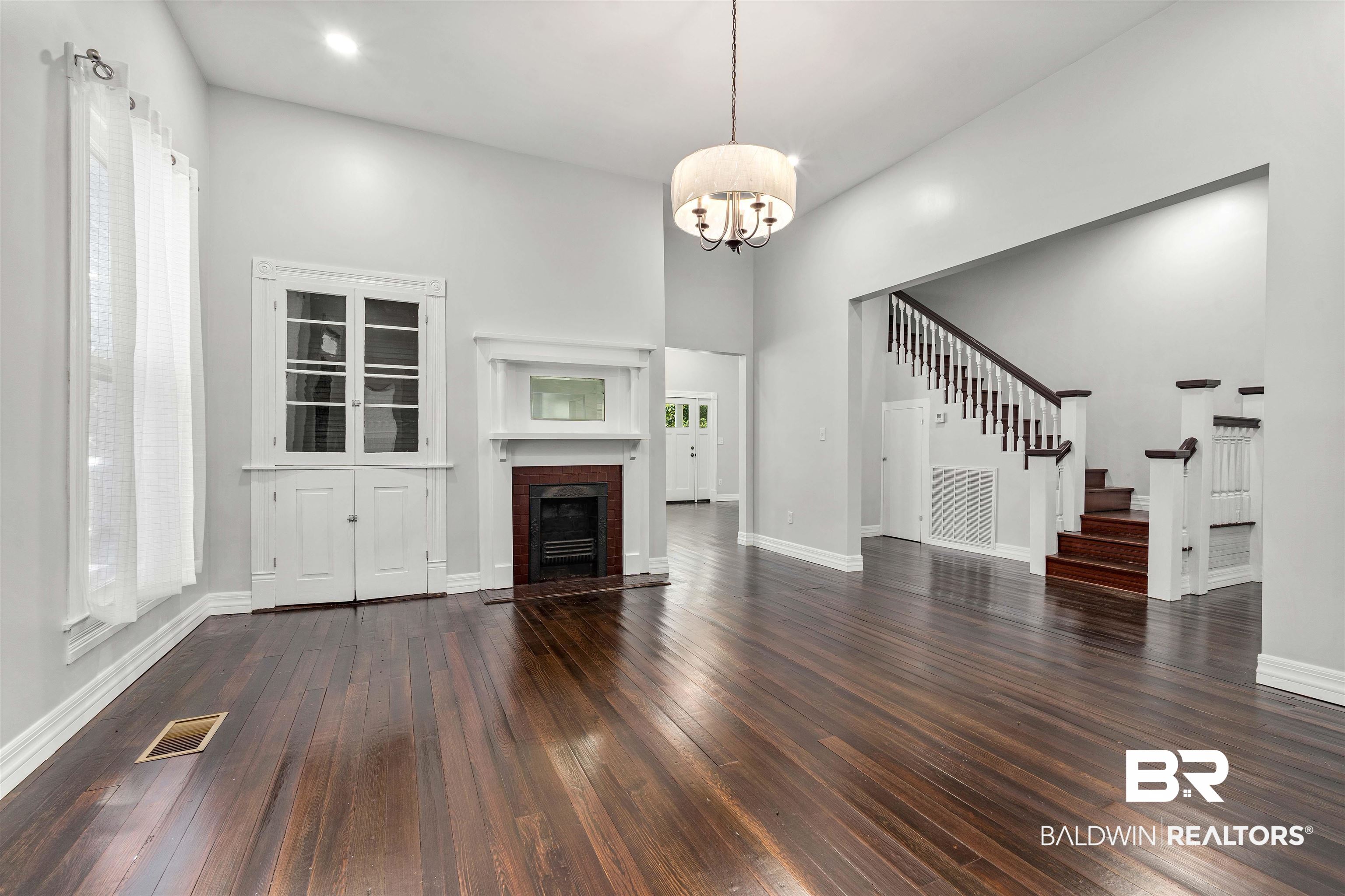 407 East 2nd Street Bay Minette, AL 36507 - Photo 12 of 40 Unfurnished living room with stairway, dark wood-style flooring, a high ceiling, a fireplace with flush hearth, and a chandelier