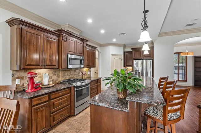 a kitchen with stainless steel appliances kitchen island granite countertop a stove refrigerator and cabinets