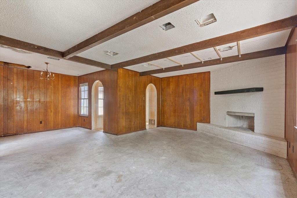 317 Chapman Road Hewitt, TX 76643 - Photo 4 of 20 Spacious room featuring wood paneling, exposed ceiling beams, an arched doorway, and a white brick fireplace with a mantel