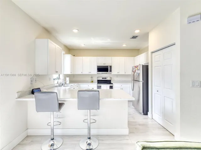 a living room with stainless steel appliances kitchen island granite countertop a refrigerator a stove a sink and a dining table with wooden floor