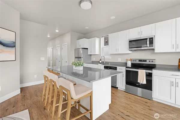 a kitchen with stainless steel appliances kitchen island granite countertop a stove a sink a refrigerator and white cabinets with wooden floor