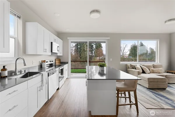 a large kitchen with kitchen island a large window cabinets a sink and stainless steel appliances
