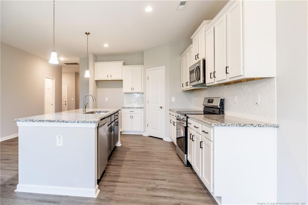 260 Carolina Church Road St. Pauls, NC 28384 - Photo 22 of 32 a kitchen with stainless steel appliances granite countertop a stove top oven a sink a refrigerator and white cabinets with wooden floor