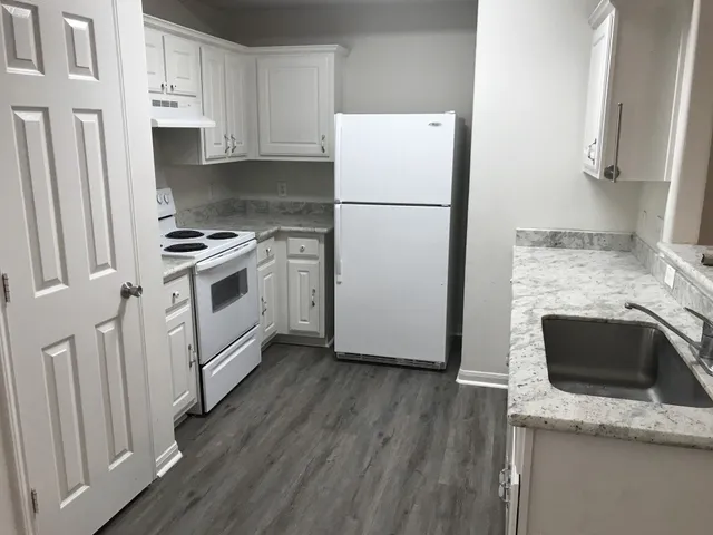 a kitchen with granite countertop a refrigerator a stove a sink and white cabinets with wooden floor