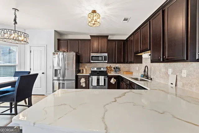 a kitchen with stainless steel appliances granite countertop a refrigerator a sink a stove a dining table and chairs with wooden floor