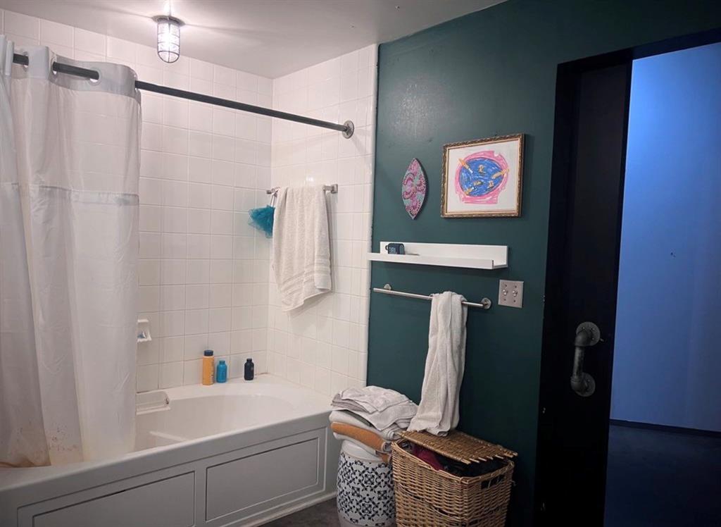 1122 Jackson Street, Unit 514 Dallas, TX 75202 - Photo 27 of 40 Bathroom featuring a white subway tile surround, a built-in tub, white paneling on the tub exterior, a dark green painted wall, and a black sliding door