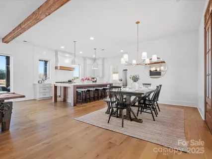 a view of a dining room and livingroom with furniture wooden floor a rug a flat screen tv a painting and a chandelier