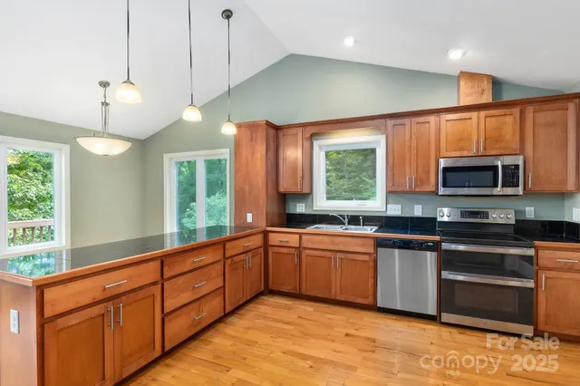 a kitchen with stainless steel appliances granite countertop wooden cabinets a stove a sink and a large window