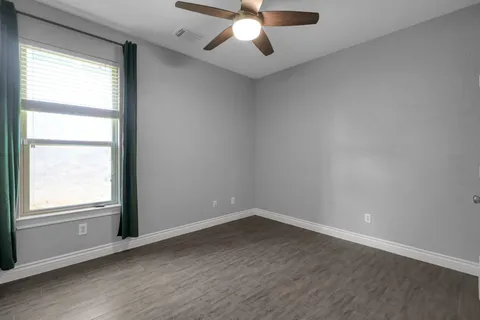 an empty room with wooden floor chandelier fan and windows