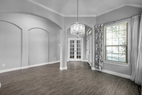 an empty room with wooden floor chandelier and windows