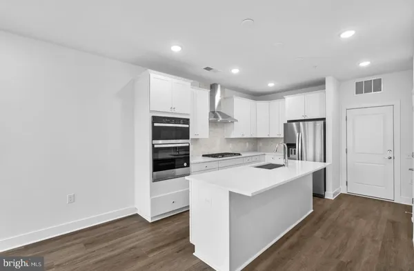 a kitchen with stainless steel appliances a stove top oven a refrigerator and white cabinets with wooden floor