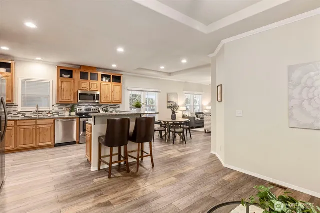 a kitchen with stainless steel appliances kitchen island granite countertop a refrigerator a stove a sink a dining table and chairs with wooden floor