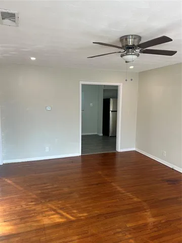 a view of an empty room with wooden floor and a ceiling fan
