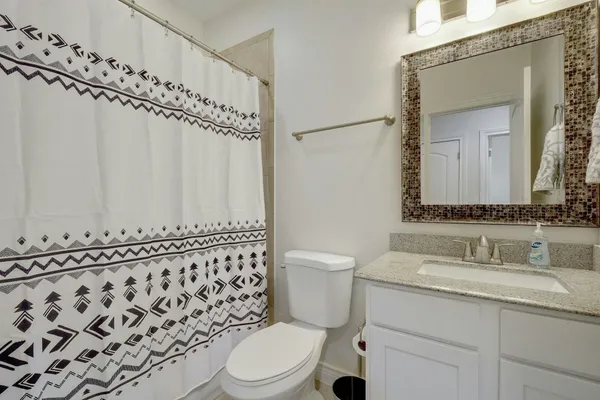 a bathroom with a granite countertop sink a toilet a mirror and shower