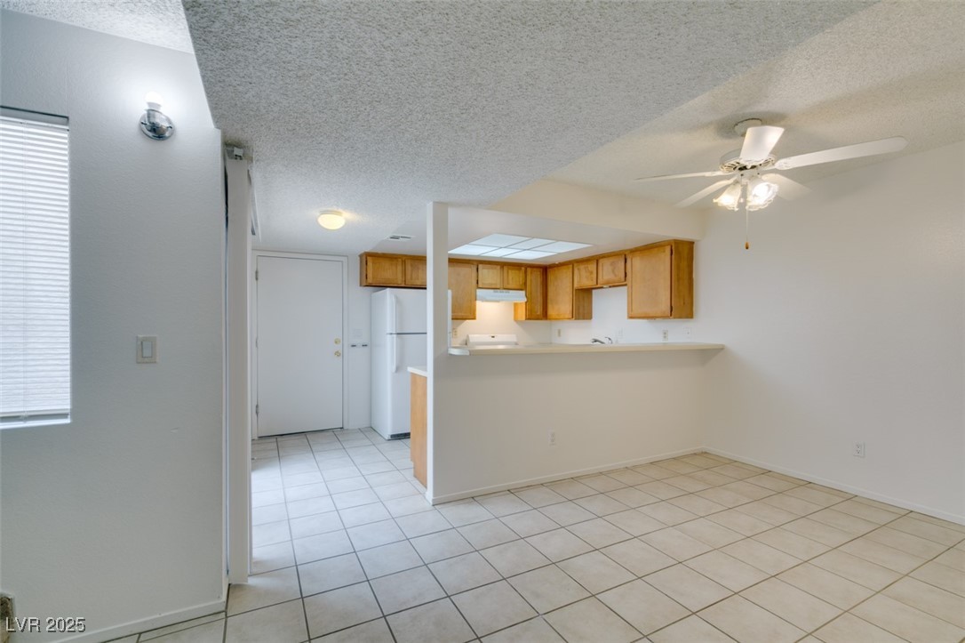 2681 Ruthe Duarte Avenue Las Vegas, NV 89121 - Photo 13 of 43 Kitchen featuring a ceiling fan, freestanding refrigerator, a peninsula, under cabinet range hood, and a textured ceiling