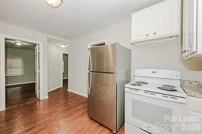 a kitchen with granite countertop a refrigerator stove and white cabinets with wooden floor
