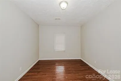 a view of an empty room with wooden floor and fan
