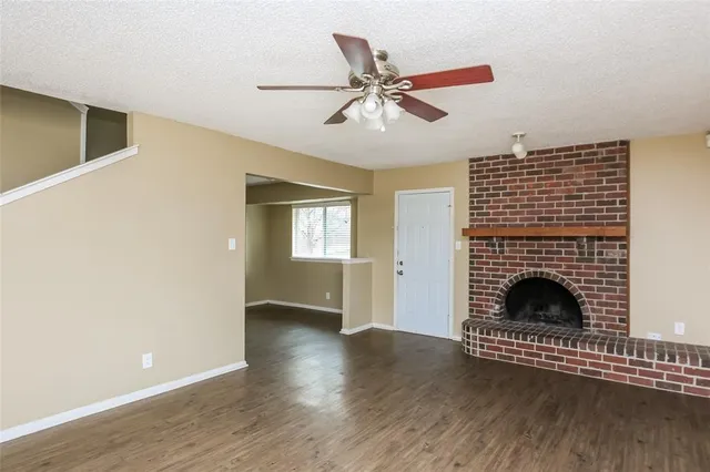 a view of an empty room with wooden floor fireplace and a window