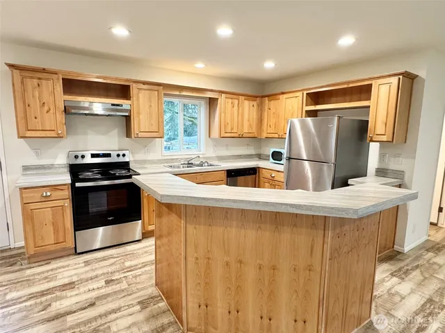 a kitchen with stainless steel appliances granite countertop a refrigerator a sink a stove and a refrigerator with wooden floor