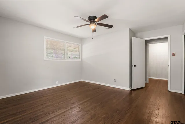 a view of an empty room with wooden floor and a ceiling fan