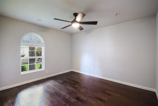 an empty room with wooden floor chandelier fan and windows