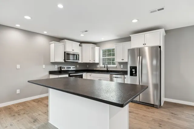 a kitchen with stainless steel appliances granite countertop a refrigerator a sink a stove a microwave a center island and wooden floor