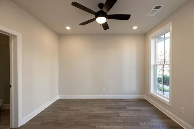 an empty room with wooden floor fan and windows