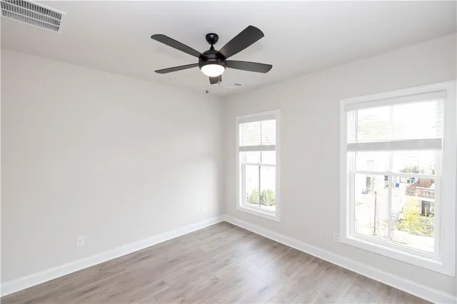 an empty room with wooden floor fan and windows