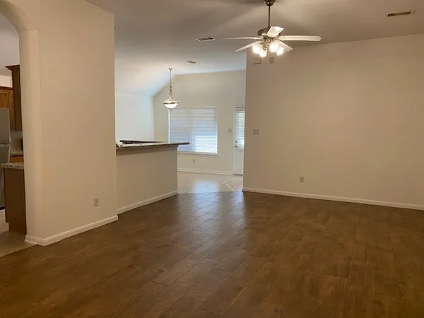 an empty room with wooden floor a ceiling fan and kitchen view